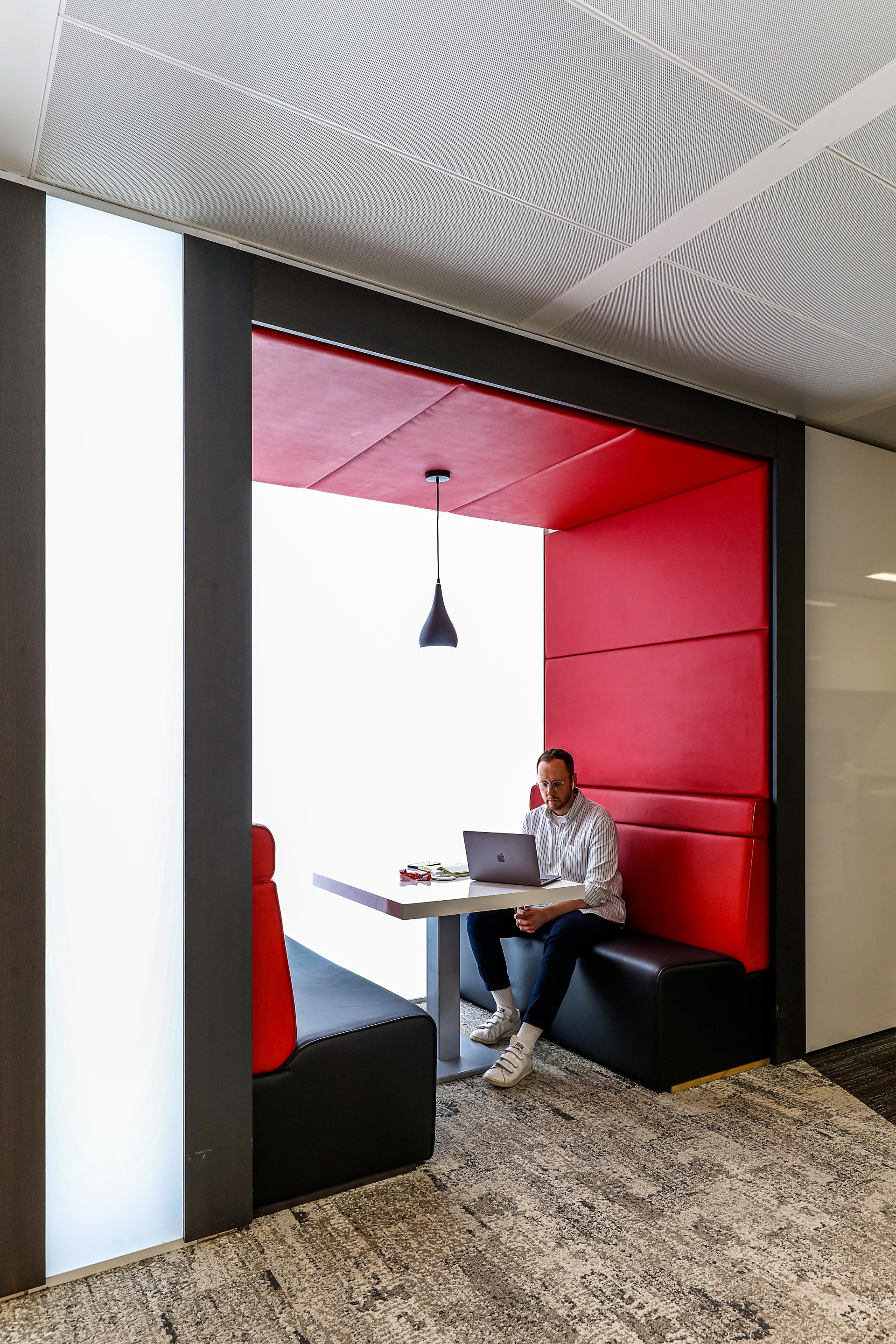 Modern workspace featuring a man working on a laptop in a low-carbon design booth with red accents.