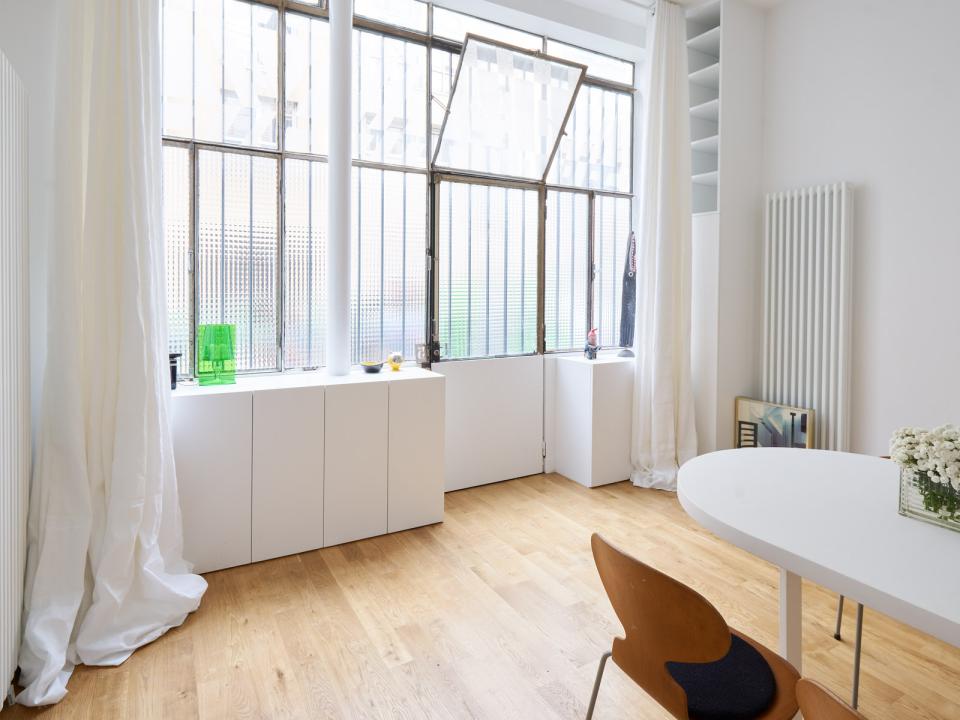 Bright, airy Parisian living space featuring large windows, wooden flooring, and minimalist furniture for flexible living.