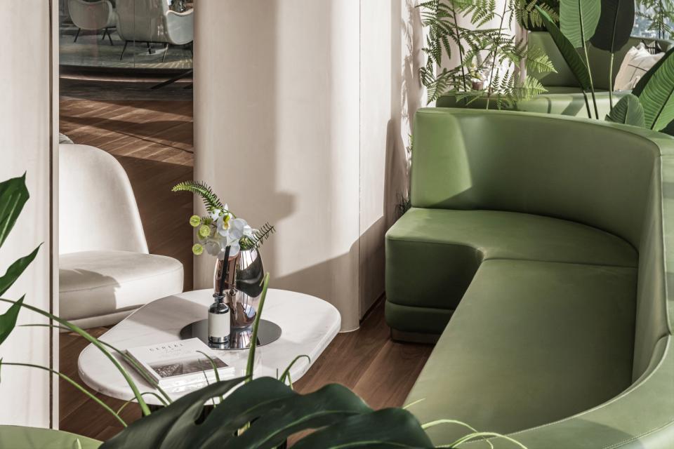 A modern workspace featuring a green curved sofa, decorative plants, and a stylish coffee table in Wenzhou City.
