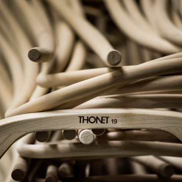 Stacked wooden chair frames with a focus on a Thonet logo, highlighting craftsmanship in Germany's production facilities.