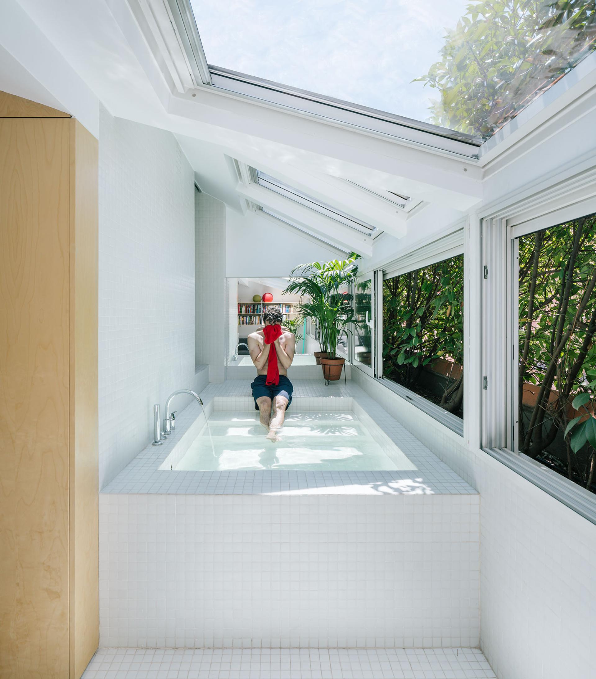 Oversized bathtub in a modern attic space, featuring large windows and a surrounding greenery view.