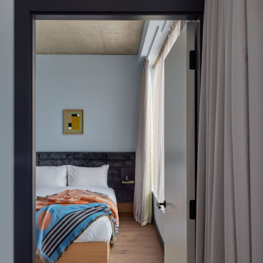 Stylish bedroom at Beckett Locke aparthotel featuring a cozy bed, decorative blanket, and natural light.