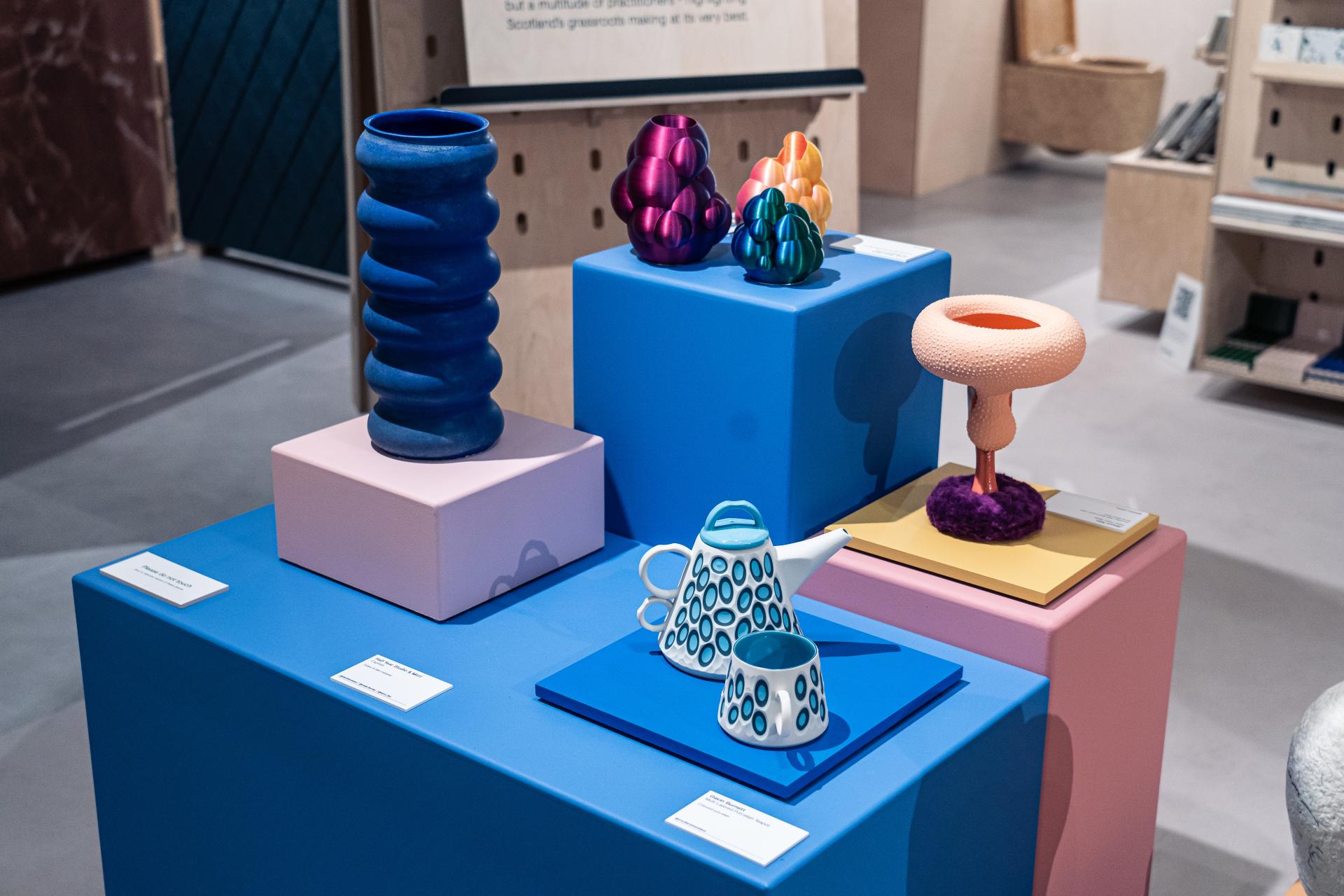 Colorful ceramic and glass sculptures displayed on vibrant pedestals at the Material Source Studio in Glasgow, showcasing Scottish design and craft.