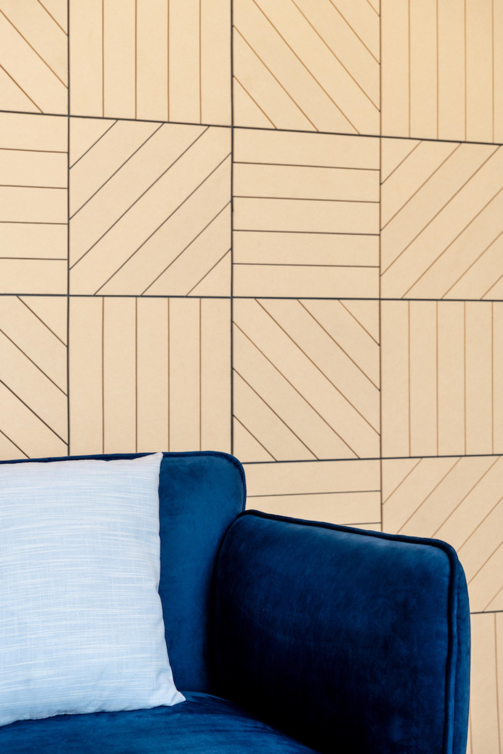 Modern design featuring a blue velvet sofa with a textured white pillow against a geometric patterned wall.