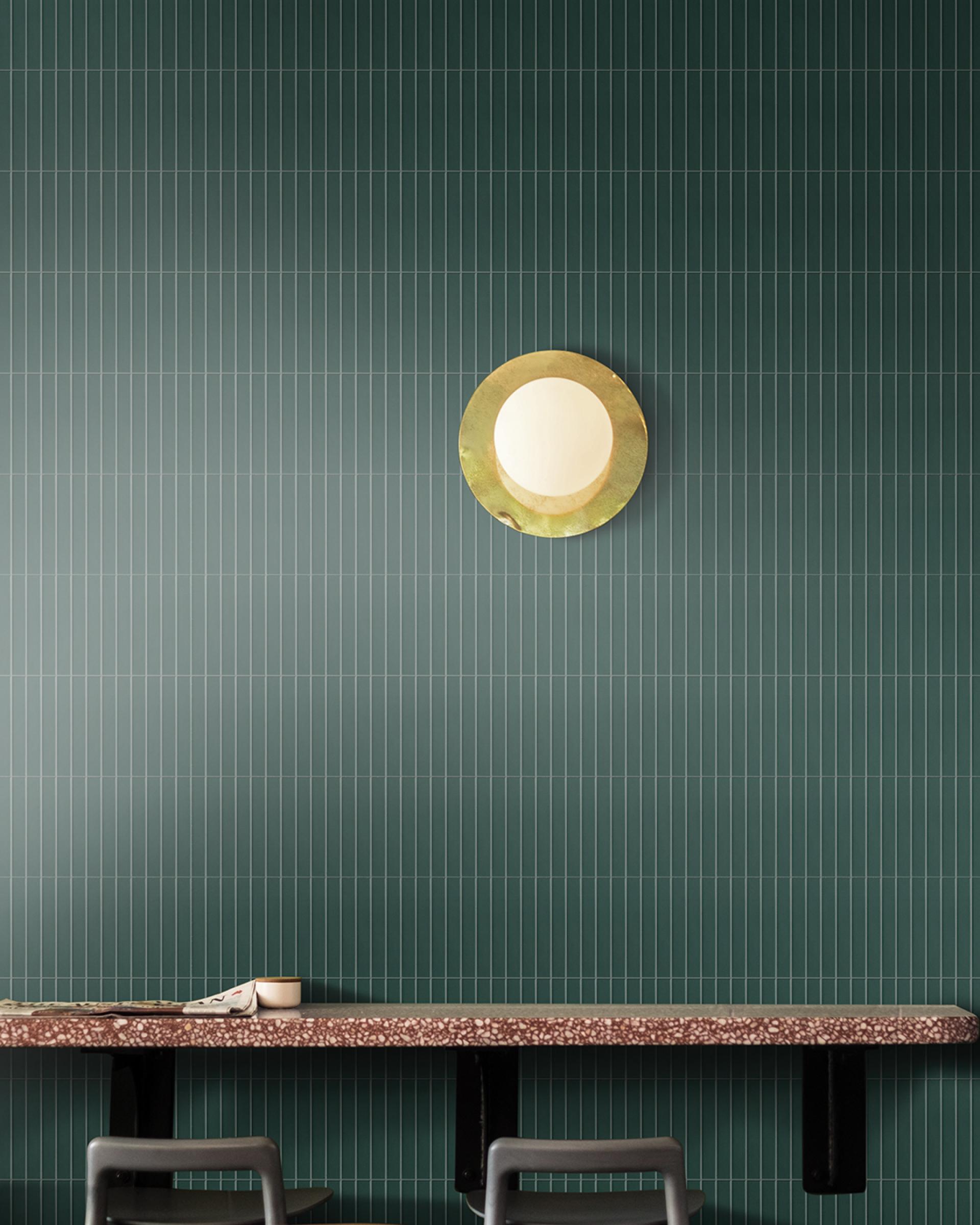 Porcelain mosaic tiles inspired by Japanese glazing techniques adorn a green wall, complemented by a round gold light fixture.