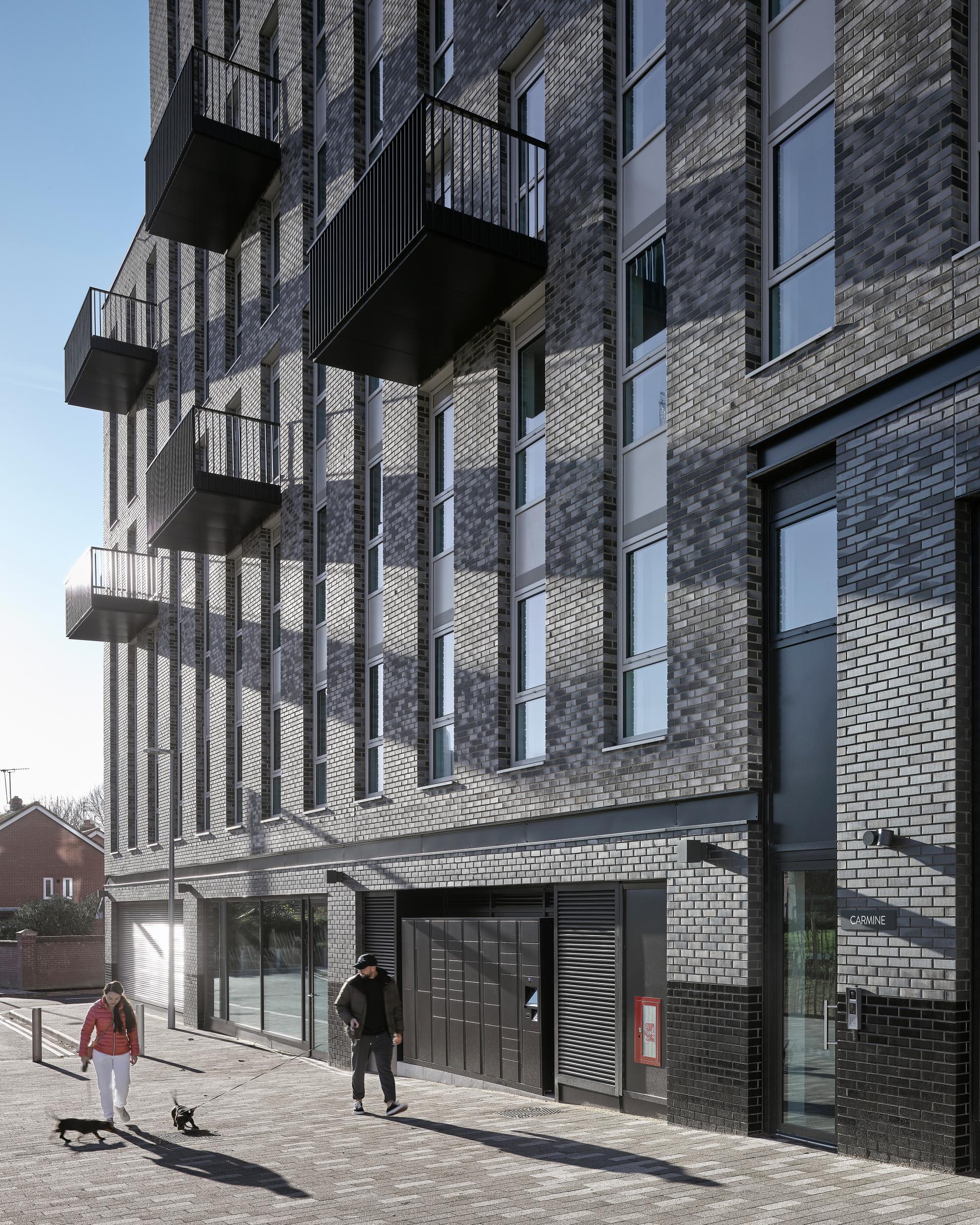 Modern urban building featuring balconies, with pedestrians walking dogs along a sunlit street, highlighting contemporary design.