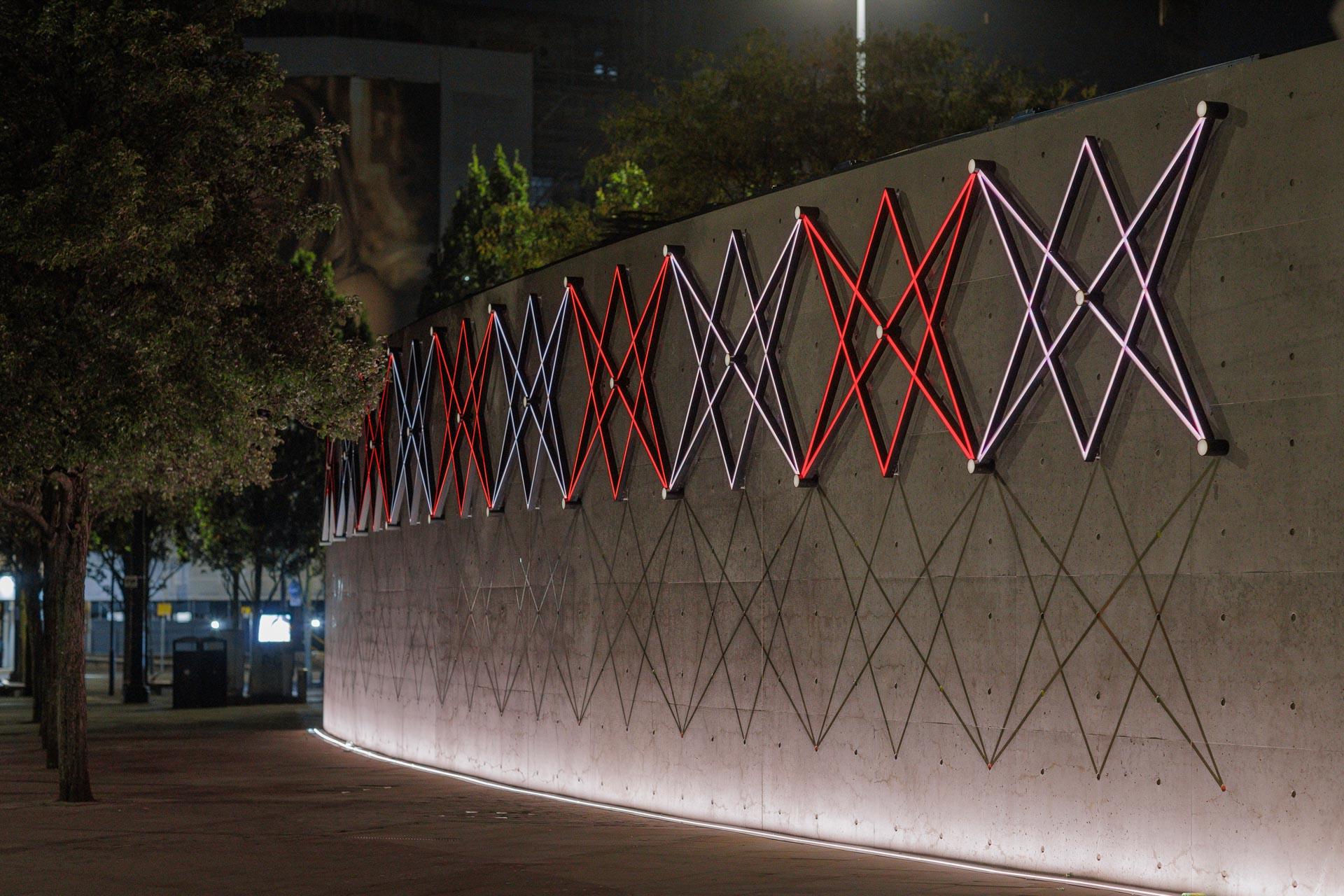 Neon light installations adorn the facade of Manchester's Piccadilly Gardens Pavilion, enhancing its modern aesthetic at night.