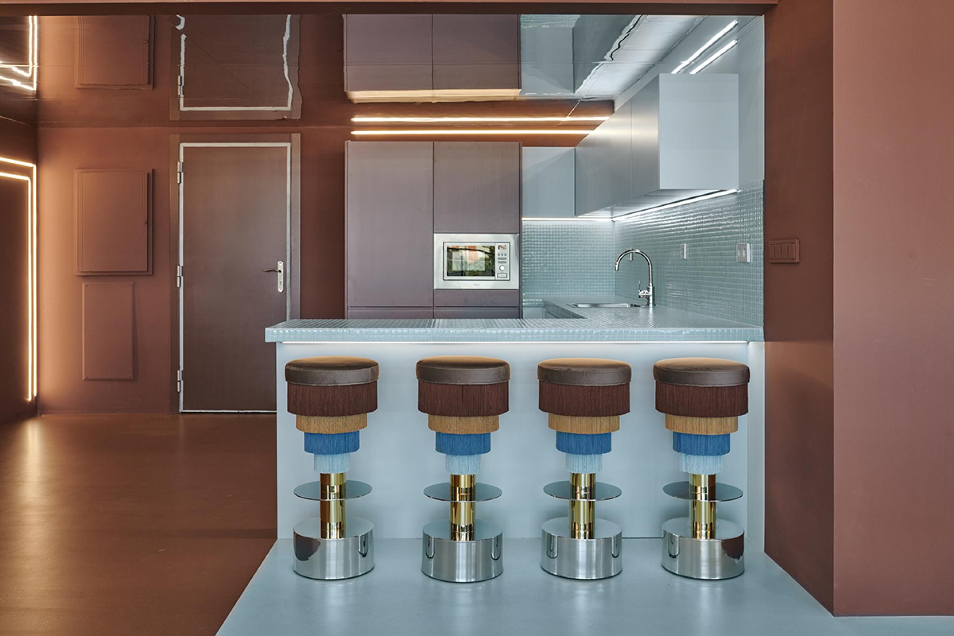Stylish coworking kitchen area in Valencia featuring modern design, colorful bar stools, and sleek cabinetry.