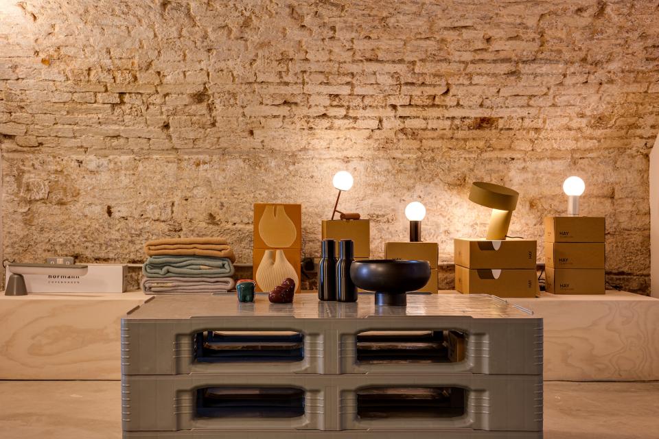 Modern interior design display featuring stylish lamps, textiles, and decor items arranged on a textured wall backdrop.