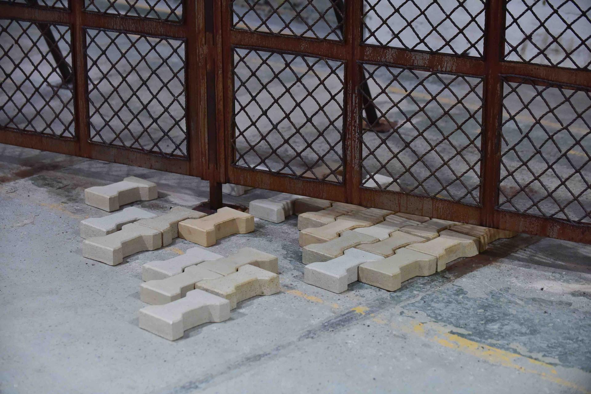Installation by Tana West featuring textured blocks and a rusty metal gate, symbolizing barriers in Europe.