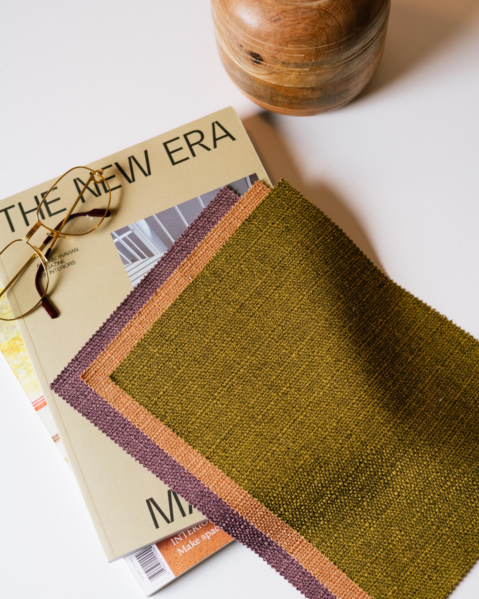 Soft performance upholstery samples in green, orange, and purple displayed alongside a modern design magazine and reading glasses.
