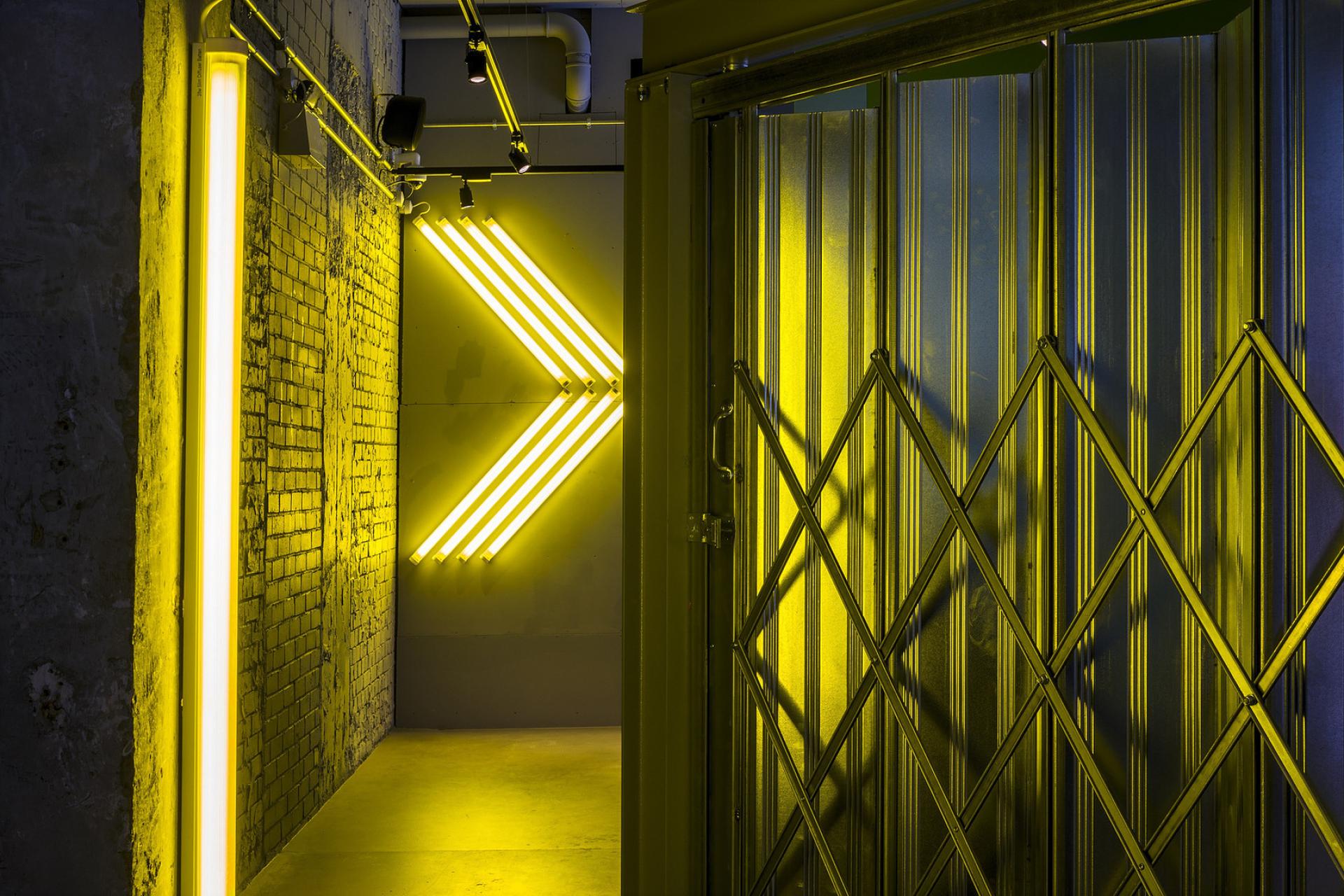 Illuminated hallway featuring striking yellow neon lighting and a textured metal door, enhancing modern design aesthetics.