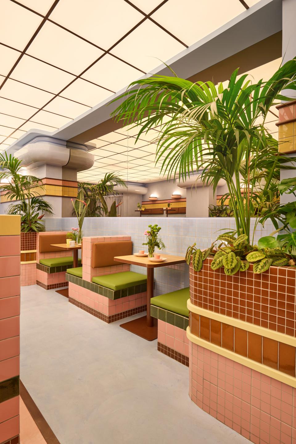 Vibrant interior of a candy-colored ice cream parlour featuring Art Deco elements, lush plants, and tiled seating areas.