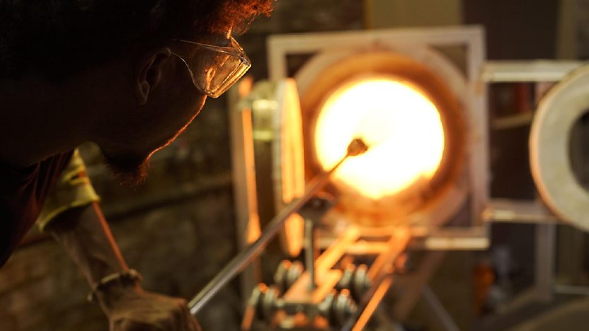 A glassblower carefully shapes molten glass in a vibrant workshop, showcasing Manchester's vibrant craft scene.