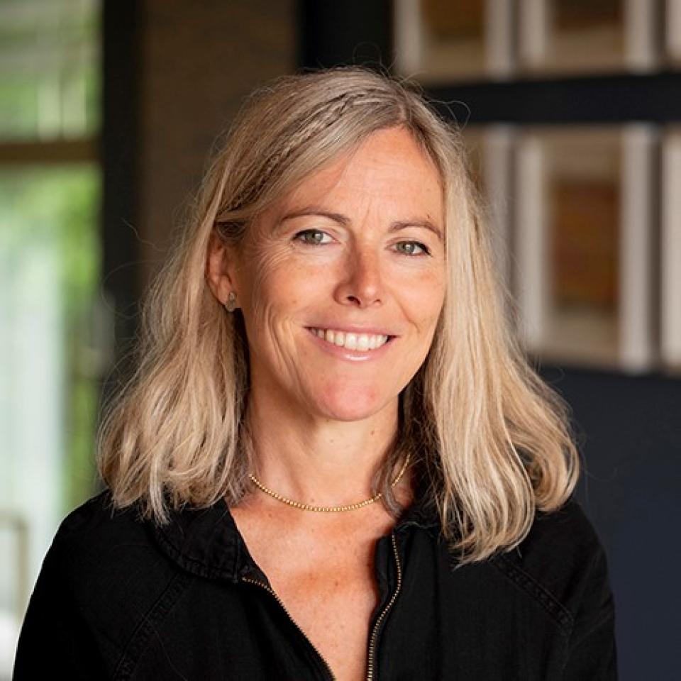 Ella Doran, designer and photographer, smiles in a creative studio with artwork in the background.