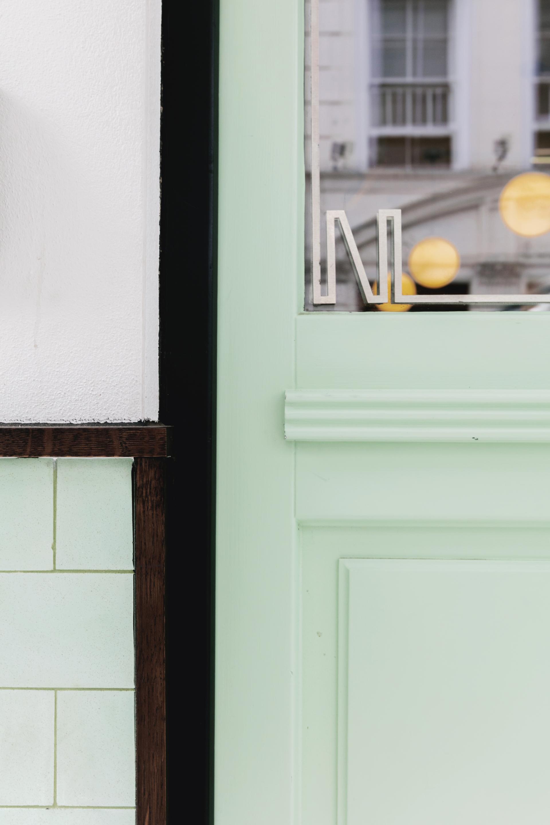 Art Deco-inspired green and white entrance door detail of Lina Stores restaurant in Soho, showcasing unique interior design elements.