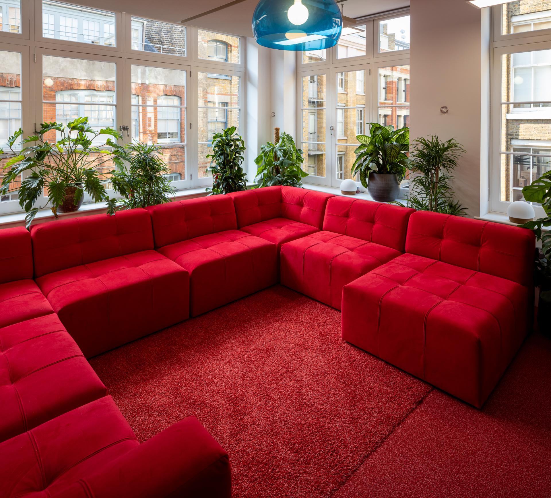 Vibrant red sectional sofa in a bright workspace surrounded by lush green plants and large windows, enhancing creative energy.