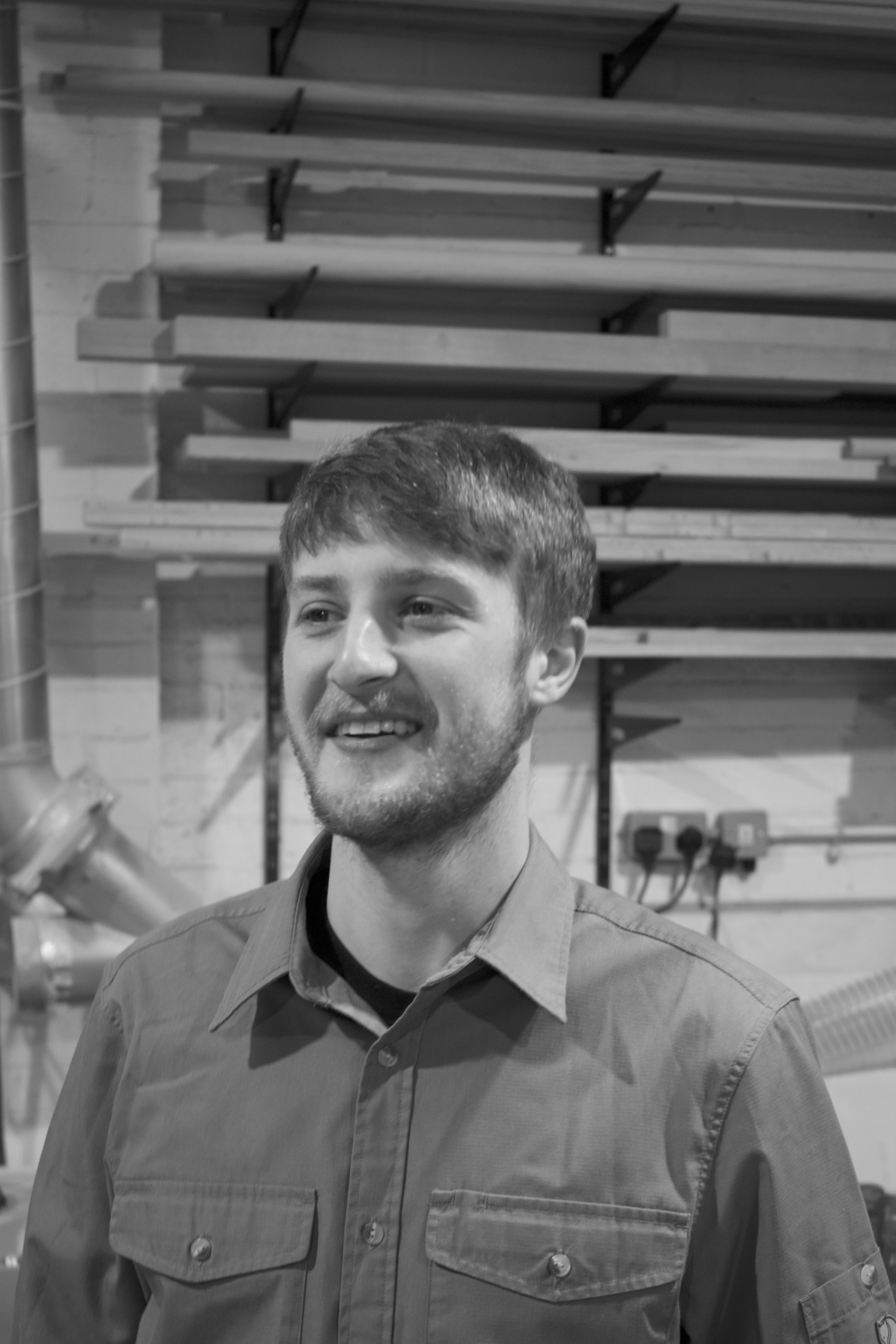 Jesse Cracknell, the maker in residence, smiling in a workshop setting with wood and tools in the background.