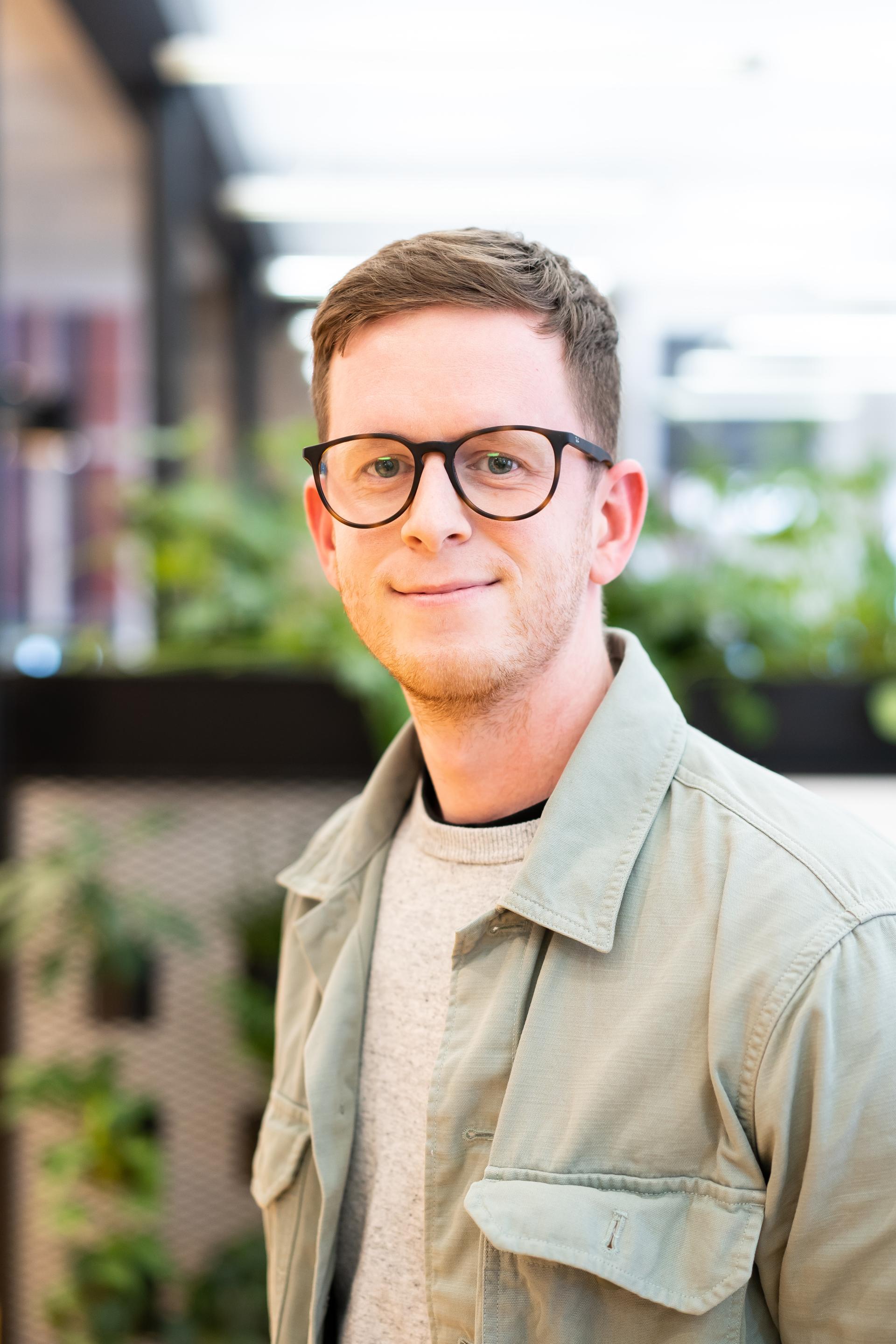 Professional smiling man wearing glasses in a modern, greenery-filled space, highlighting sustainable design solutions for the climate crisis.