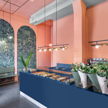 Stylish café interior featuring a navy Corian countertop, vibrant pink walls, and fresh floral arrangements.