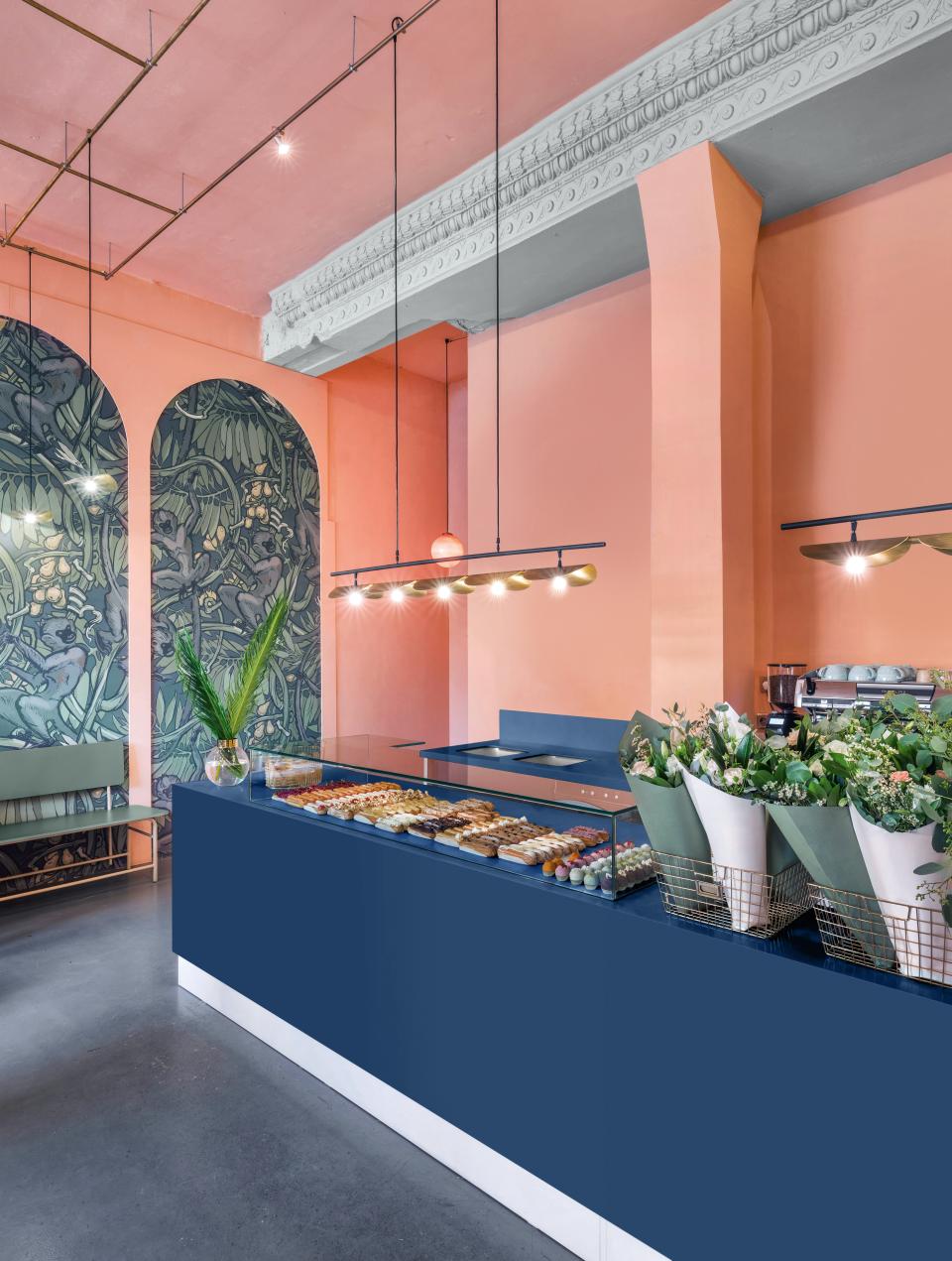 Stylish café interior featuring a navy Corian countertop, vibrant pink walls, and fresh floral arrangements.