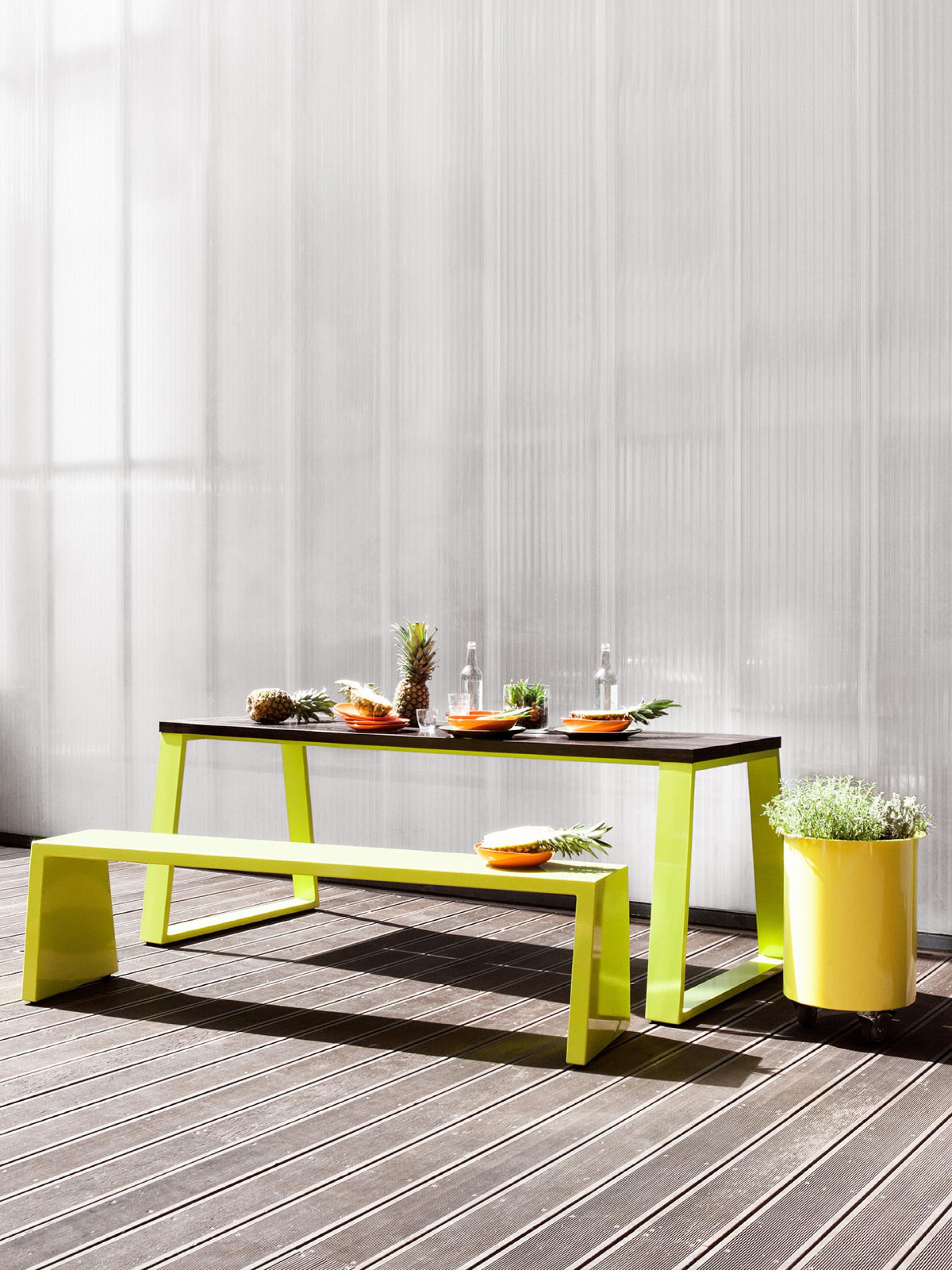 Brightly colored furniture by Jennifer Newman set outdoors, featuring a table, bench, and fresh fruit accents.