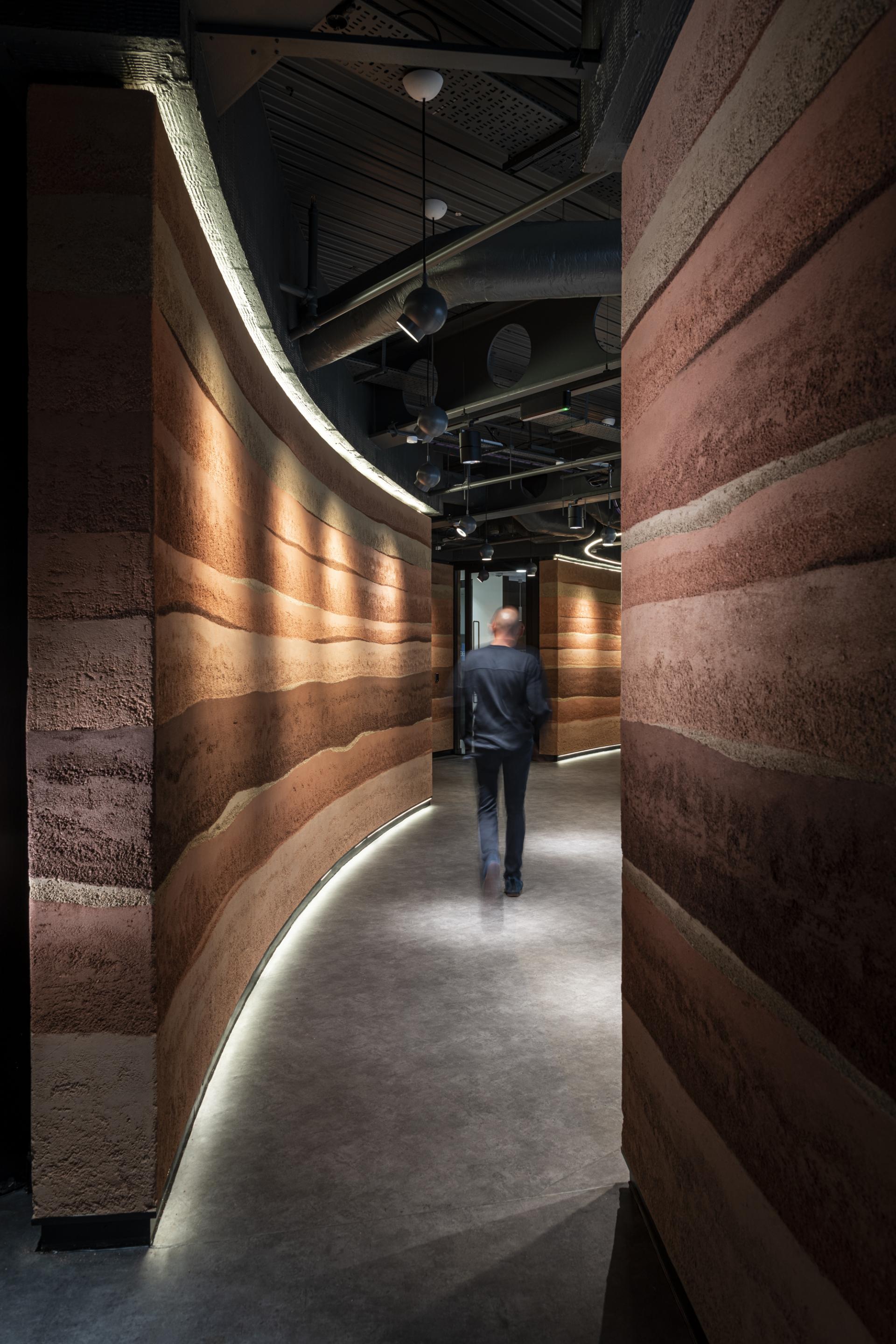Curved hallway featuring Clayworks' sustainable rammed earth wall finishes, illuminated by subtle lighting, creating a warm atmosphere.