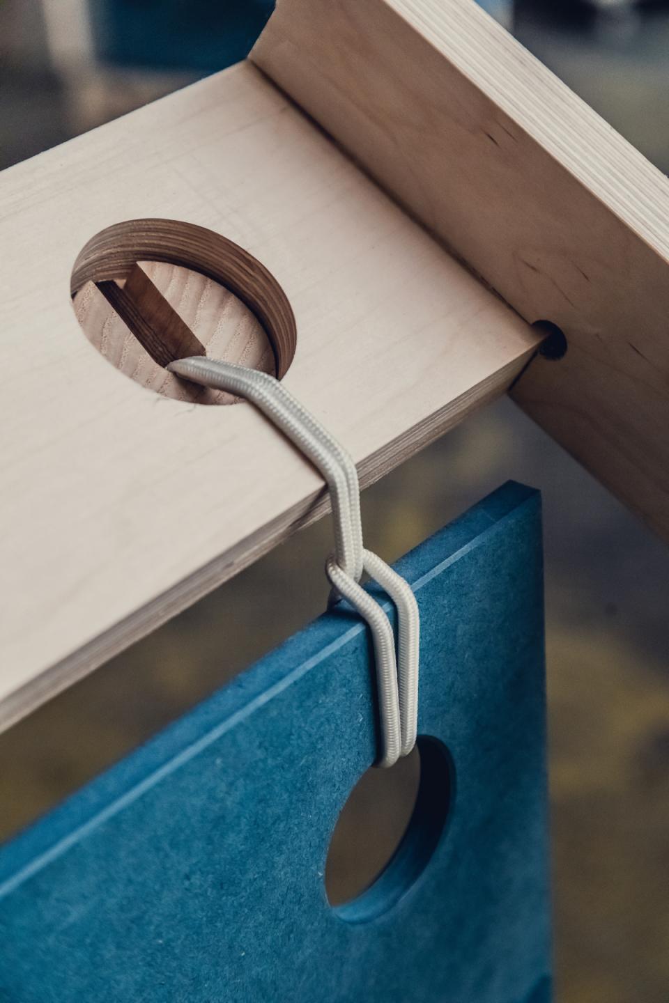 Flexible furniture system featuring wood and blue material with elastic ties, designed for pop-up shops and installations.