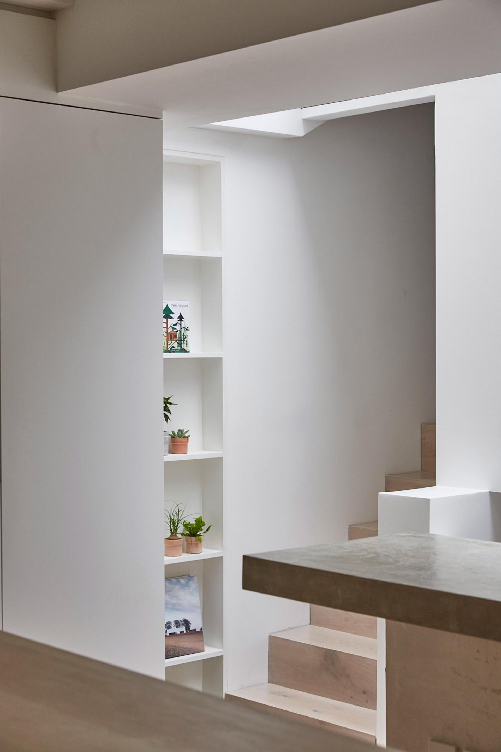 Bright, minimalist interior of a revamped mews house in Hackney, featuring built-in shelves and natural plants.
