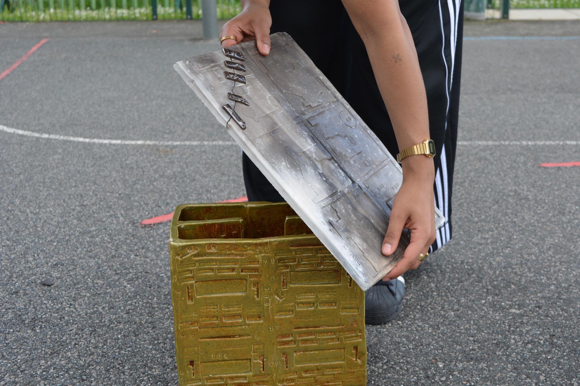 A person lifting a metal mold from a textured green container, showcasing innovative material design at New Designers 2024.
