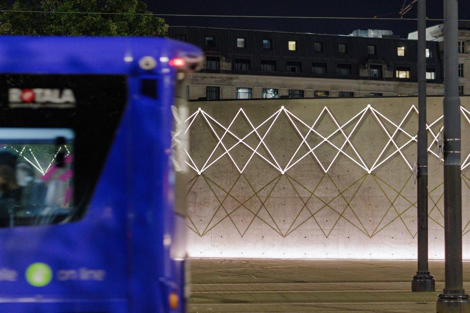 Manchester's Piccadilly Gardens Pavilion illuminated at night, featuring geometric light patterns on a concrete wall.