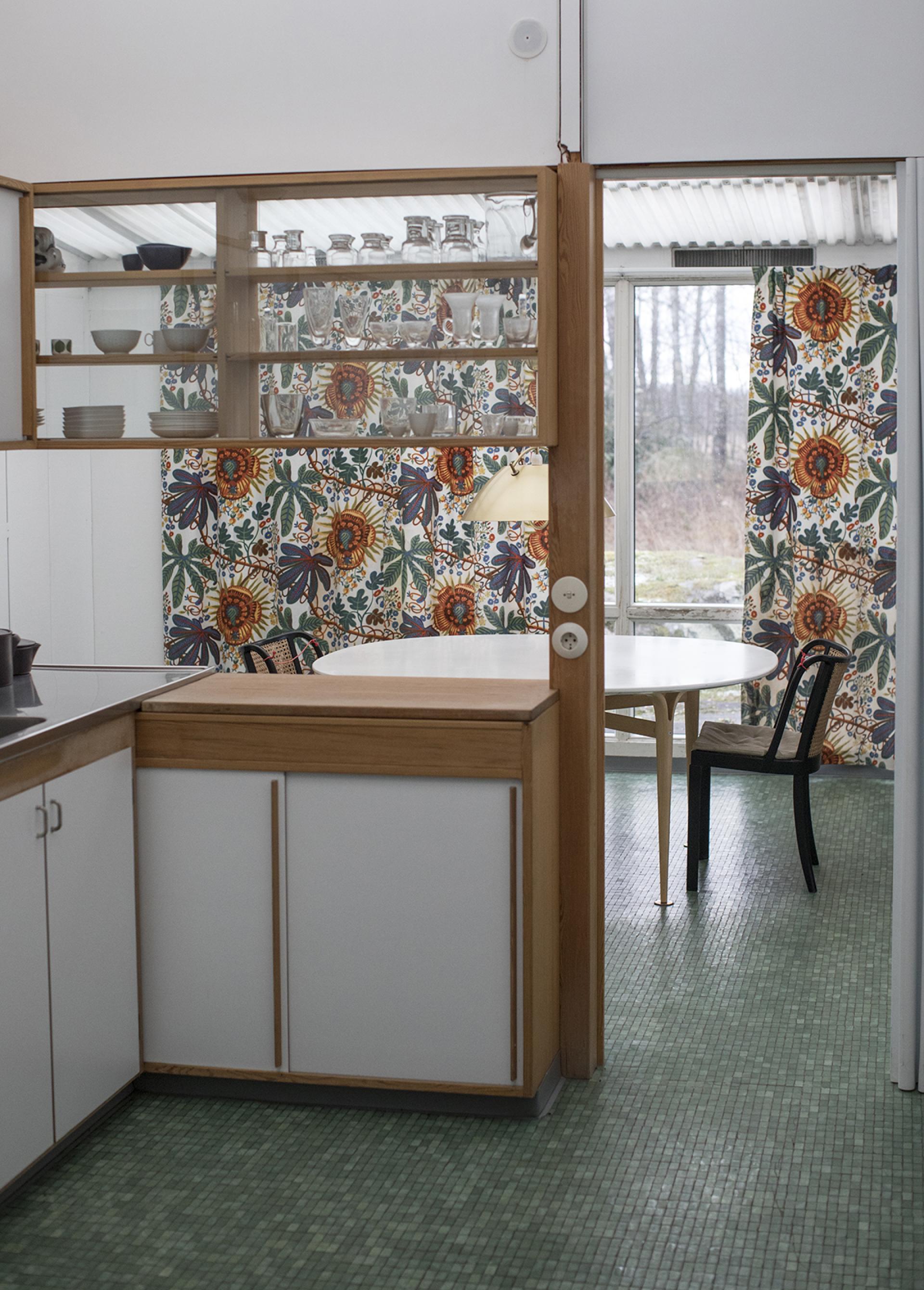 Brightly decorated kitchen in the preserved home of designer Karin Mathsson, showcasing vintage glassware and a green tiled floor.
