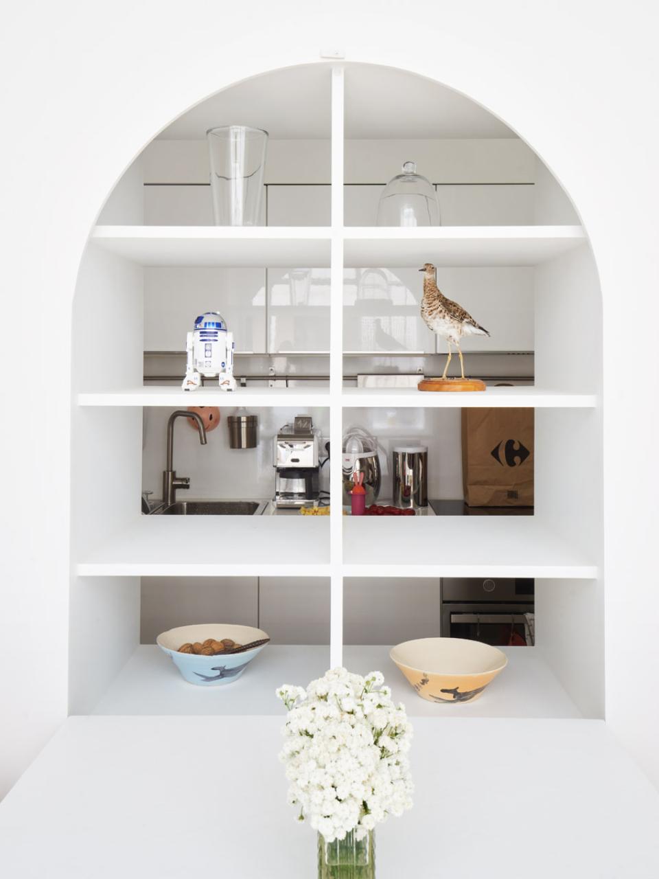 Contemporary kitchen space featuring open shelving, decorative items, and bowls, demonstrating innovative design in Parisian architecture.