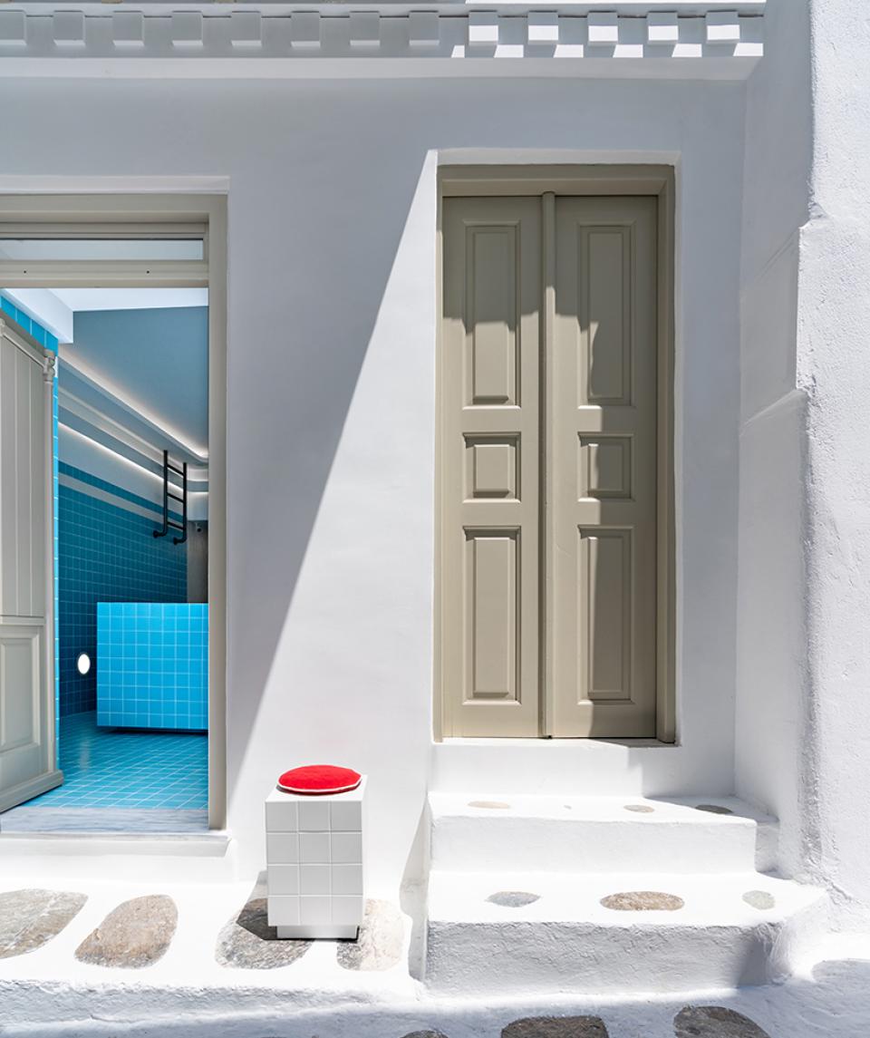 Elegant entryway featuring light-colored doors and a vibrant blue interior, embodying Wes Anderson's aesthetic in a Mykonos jewellery shop.