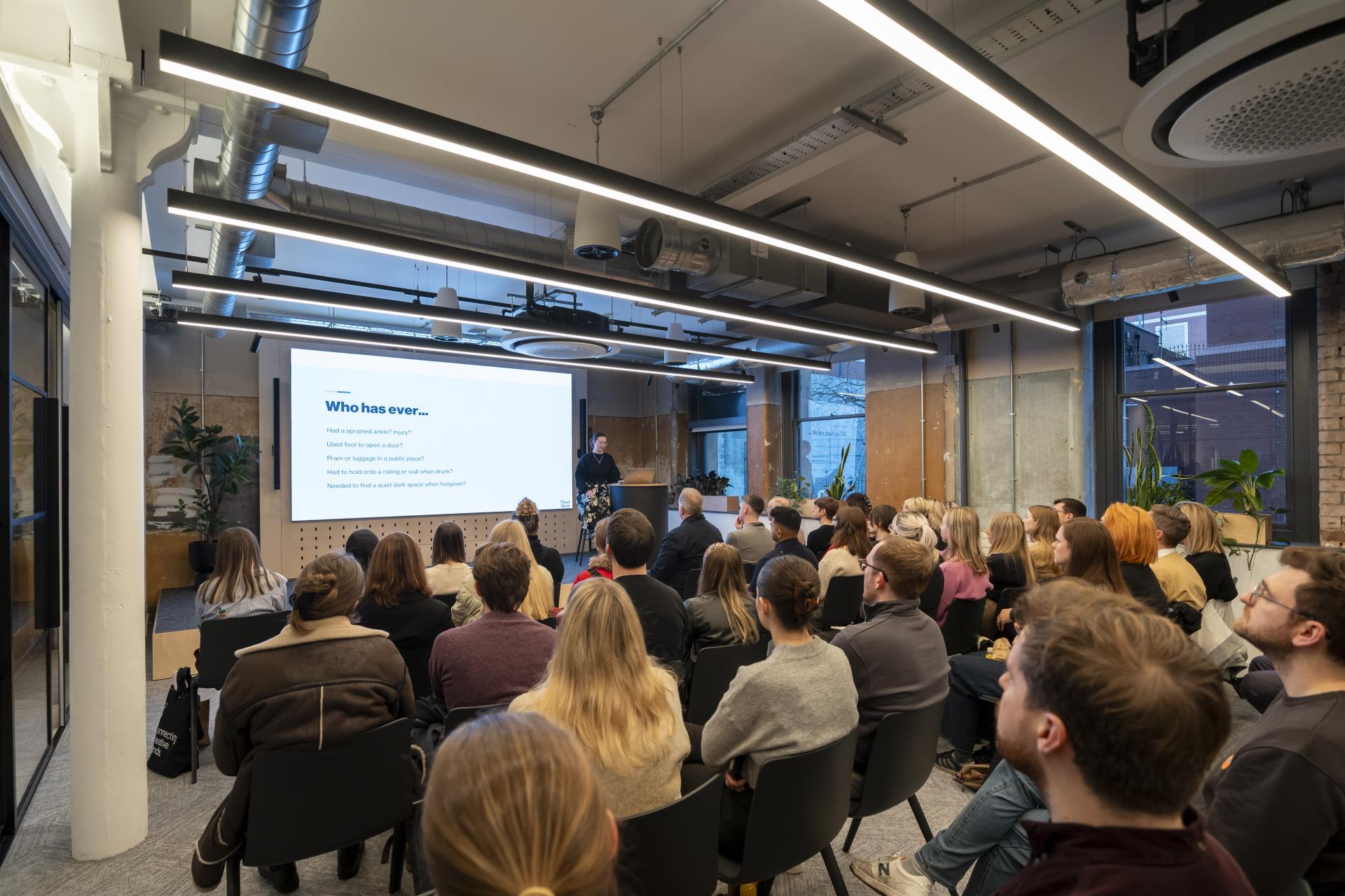 Audience listening to a presentation on neurodiversity and inclusive design, featuring a speaker and visual aids.
