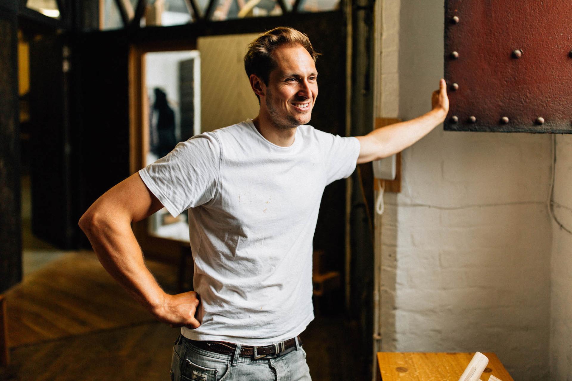 Man smiling and leaning against a wall in a creative craft studio, highlighting the artistic community in North West England.