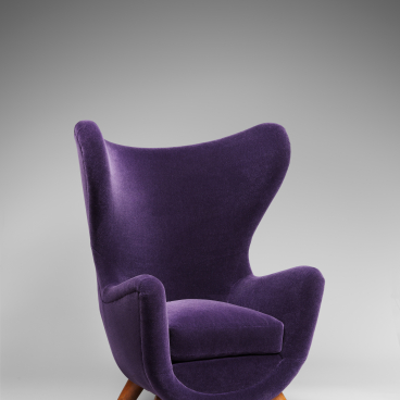 Elegant purple upholstered chair with a unique design, featuring wooden legs, highlighting mid-century modern furniture aesthetics.