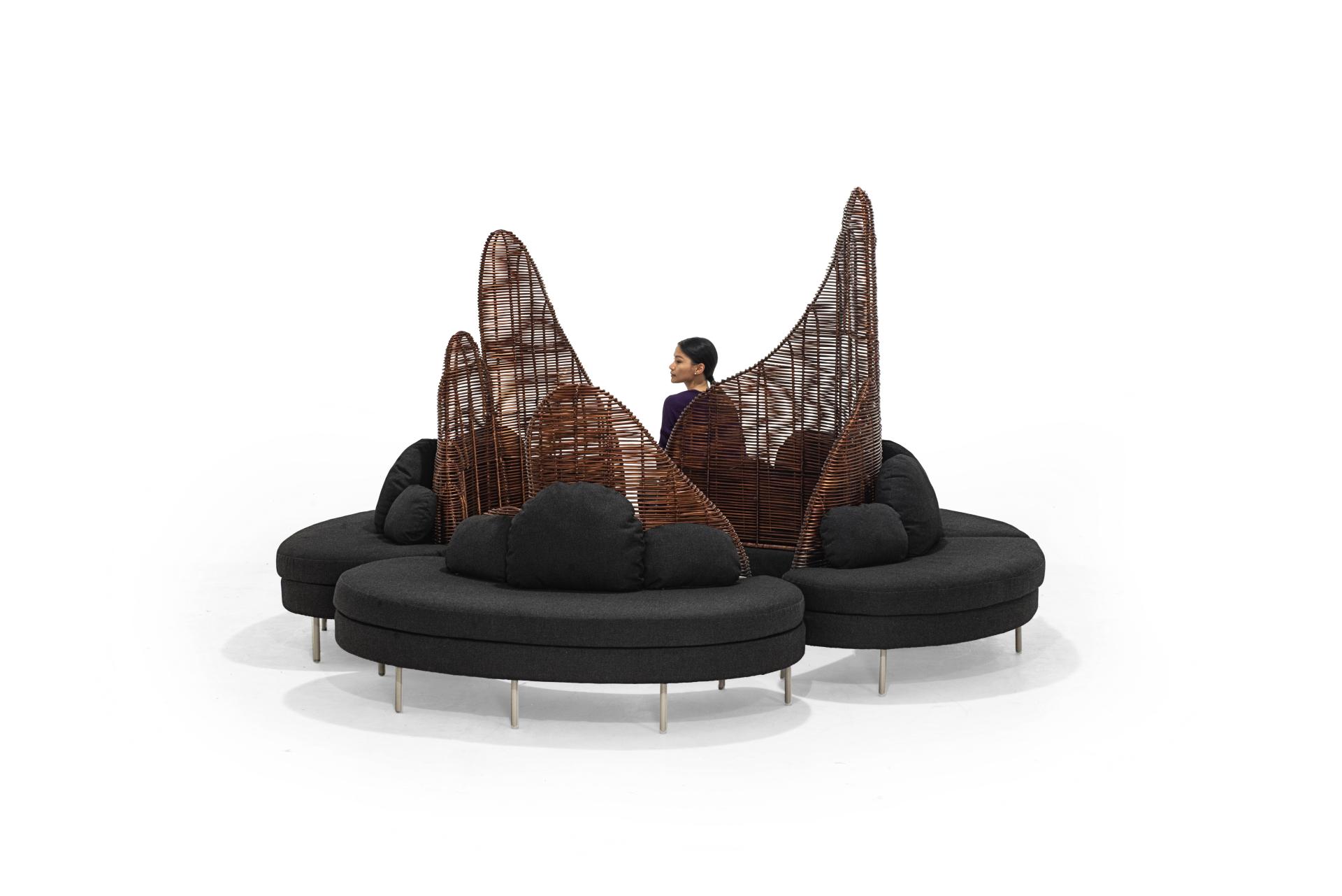 Stylish furniture piece by Kenneth Cobonpue featuring a circular design with woven backrests and plush black cushions.