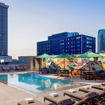 Rooftop pool area at Hyatt House Tampa featuring vibrant murals, lounge chairs, and city skyline views at dusk.