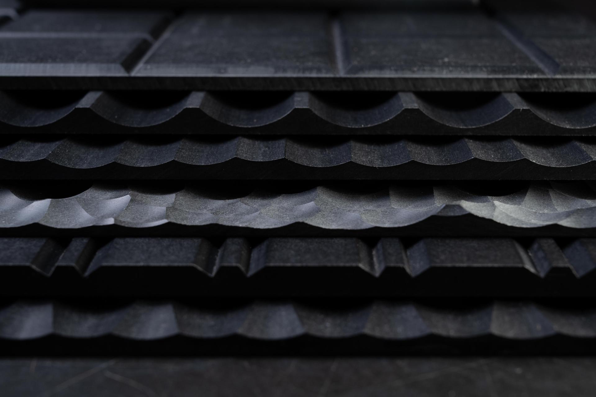 Stacked textured black materials showcasing varied wave-like patterns, highlighting Surface Matter's commitment to innovative, circular design solutions.