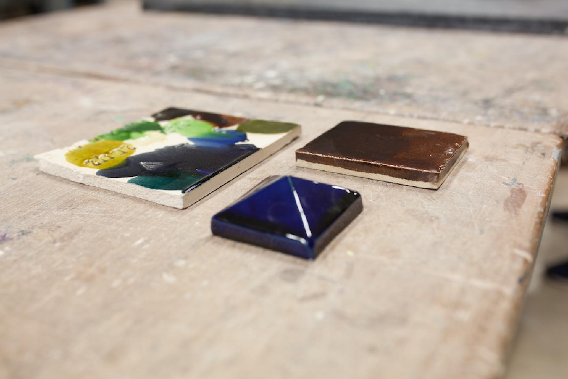 Ceramic tiles in various colors displayed on a studio worktable, highlighting Matthew Raw's artistic exploration with clay.