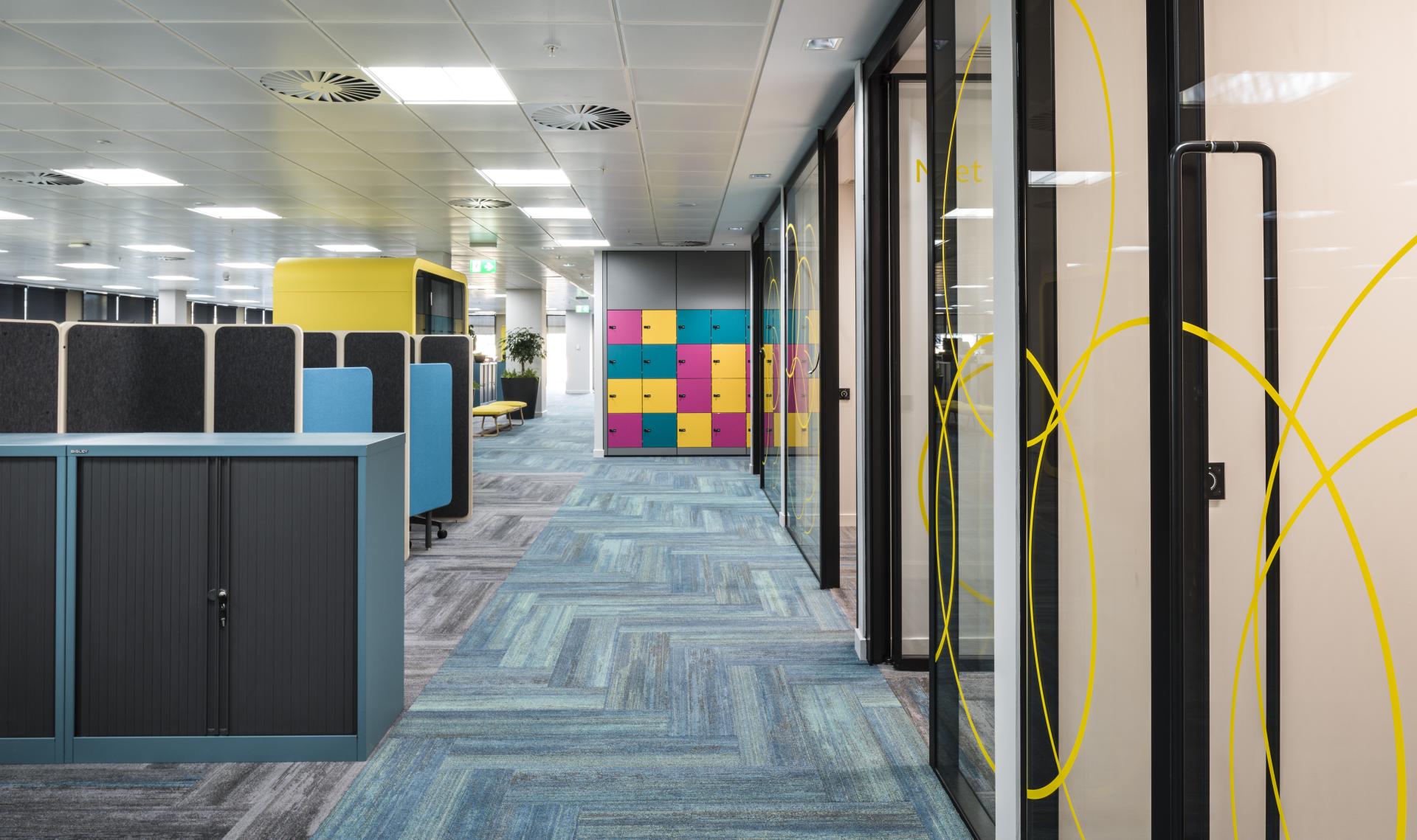 Modern office interior featuring colorful storage lockers, workspace partitions, and a stylish carpet design.