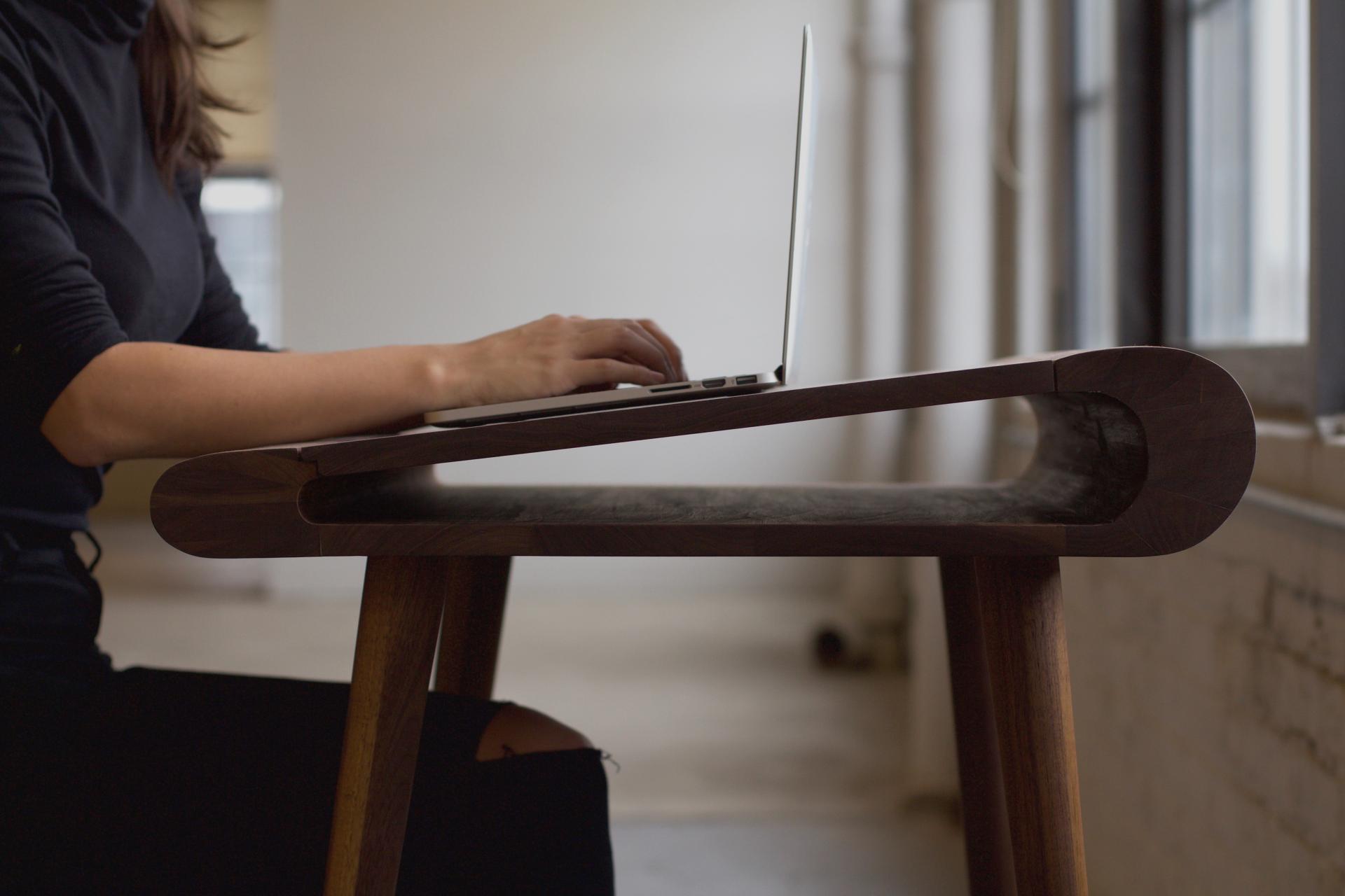 Maggie Jo Sanderson's elegant furniture design featuring a laptop on a uniquely shaped wooden desk in a modern workspace.