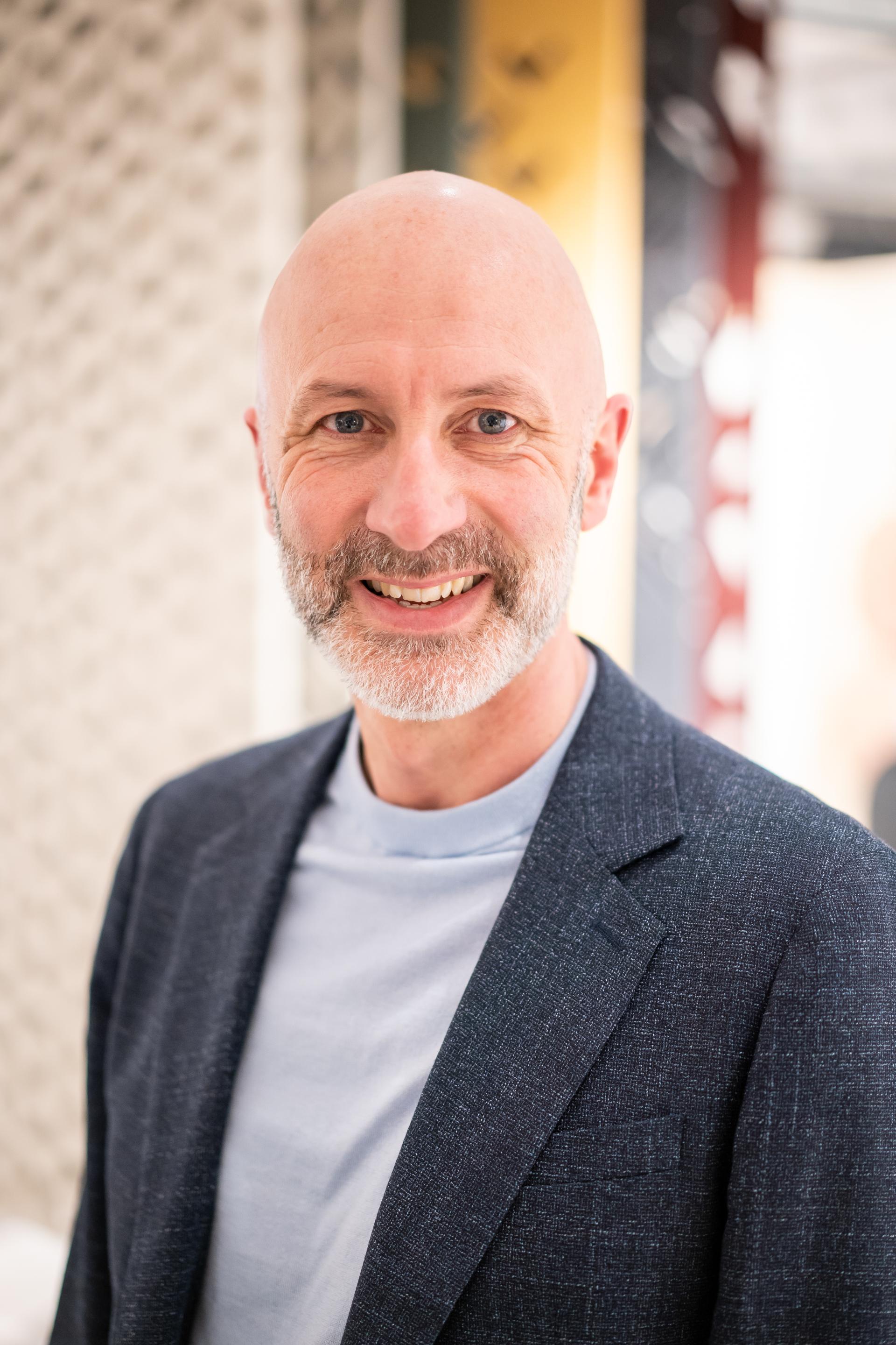 Smiling man in a blazer, representing themes of sustainability and community engagement at a seminar event.