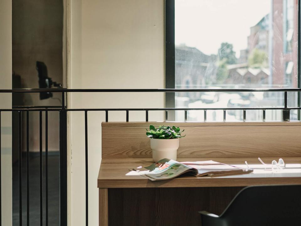 Modern workspace in The Tannery featuring a wooden desk, potted plant, and natural light from large windows.