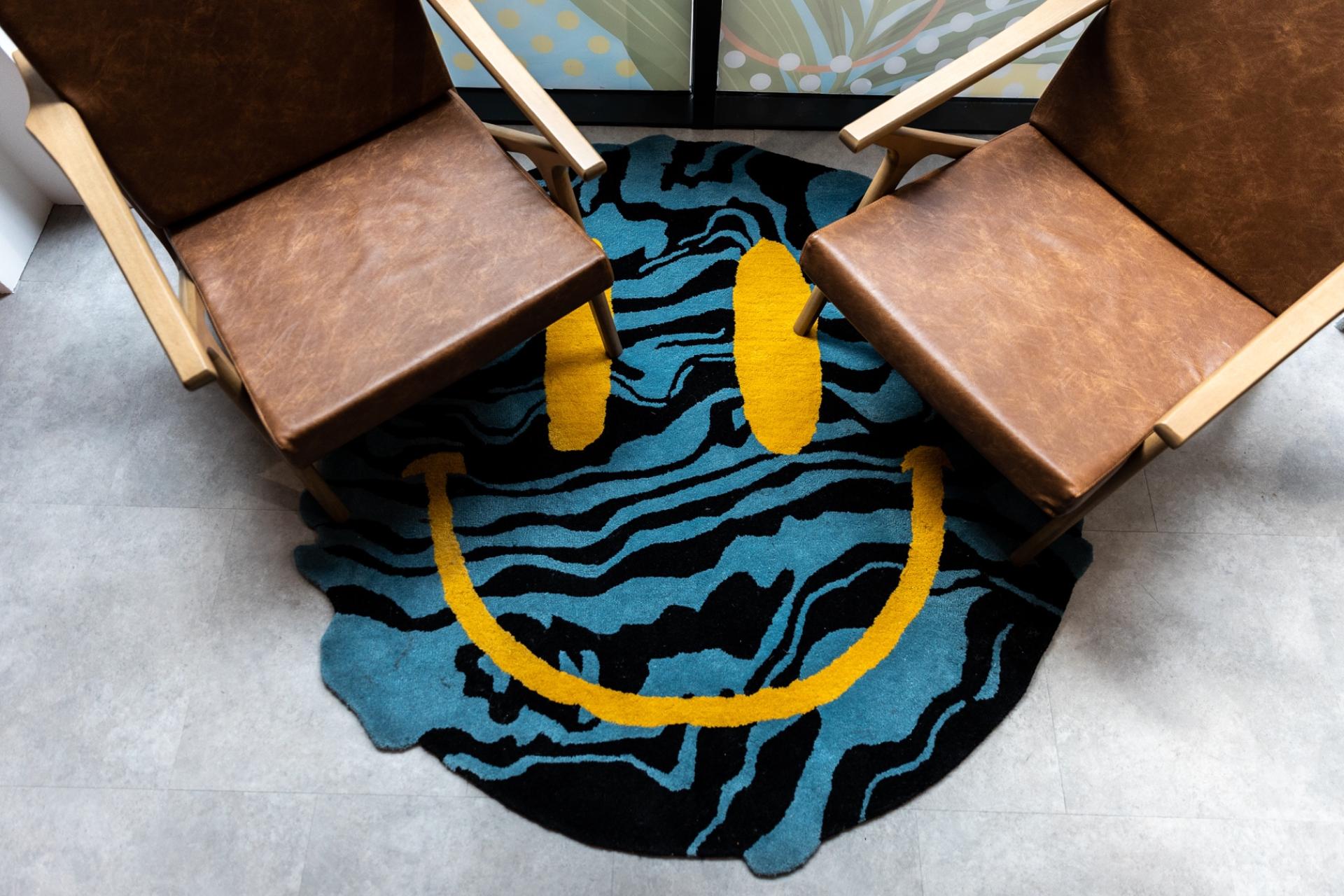 Vibrant rug with a smiley face design beneath two stylish wooden chairs in a creative workspace.