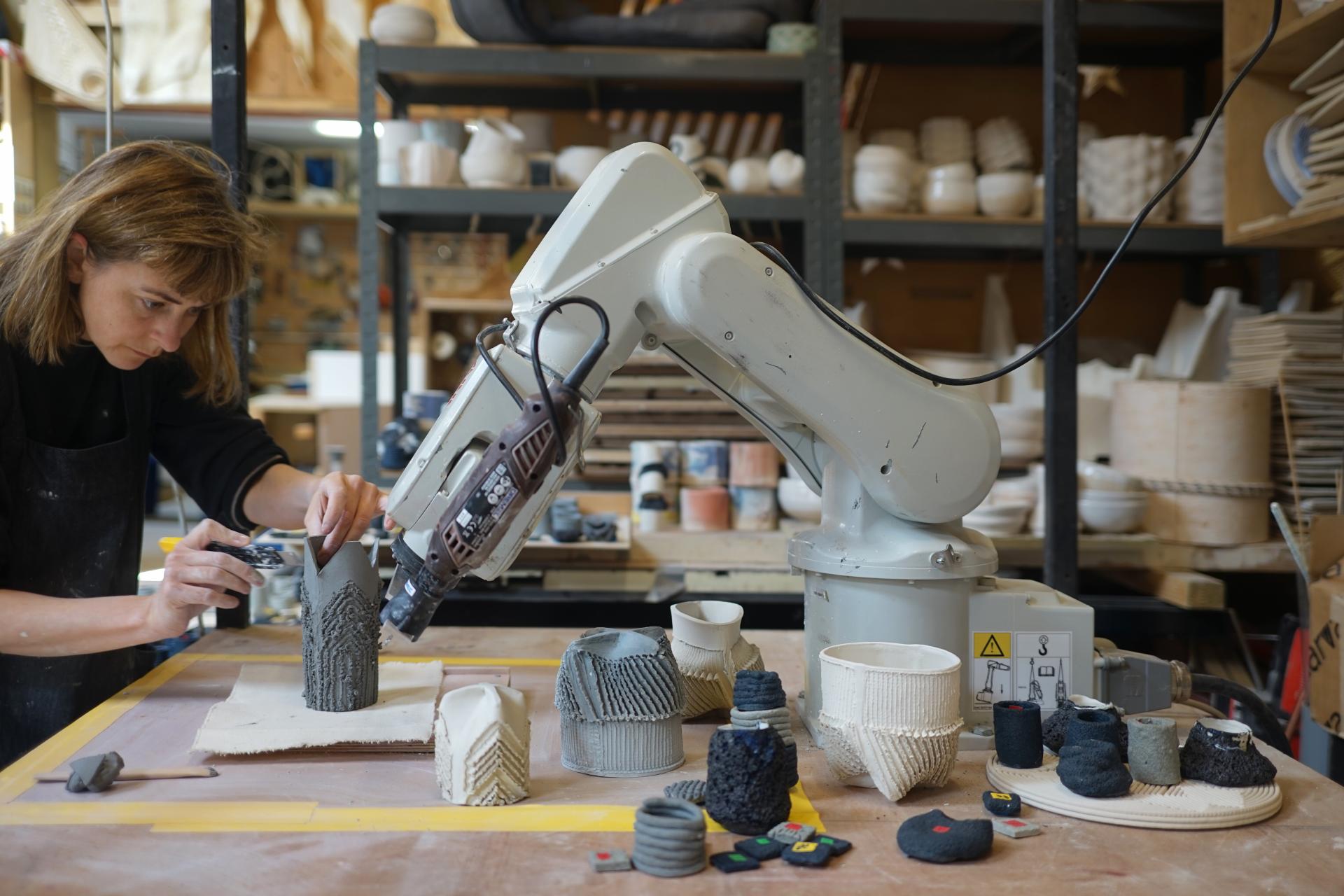 Artist utilizing a robotic arm to create intricate ceramic designs in a contemporary workshop filled with pottery.