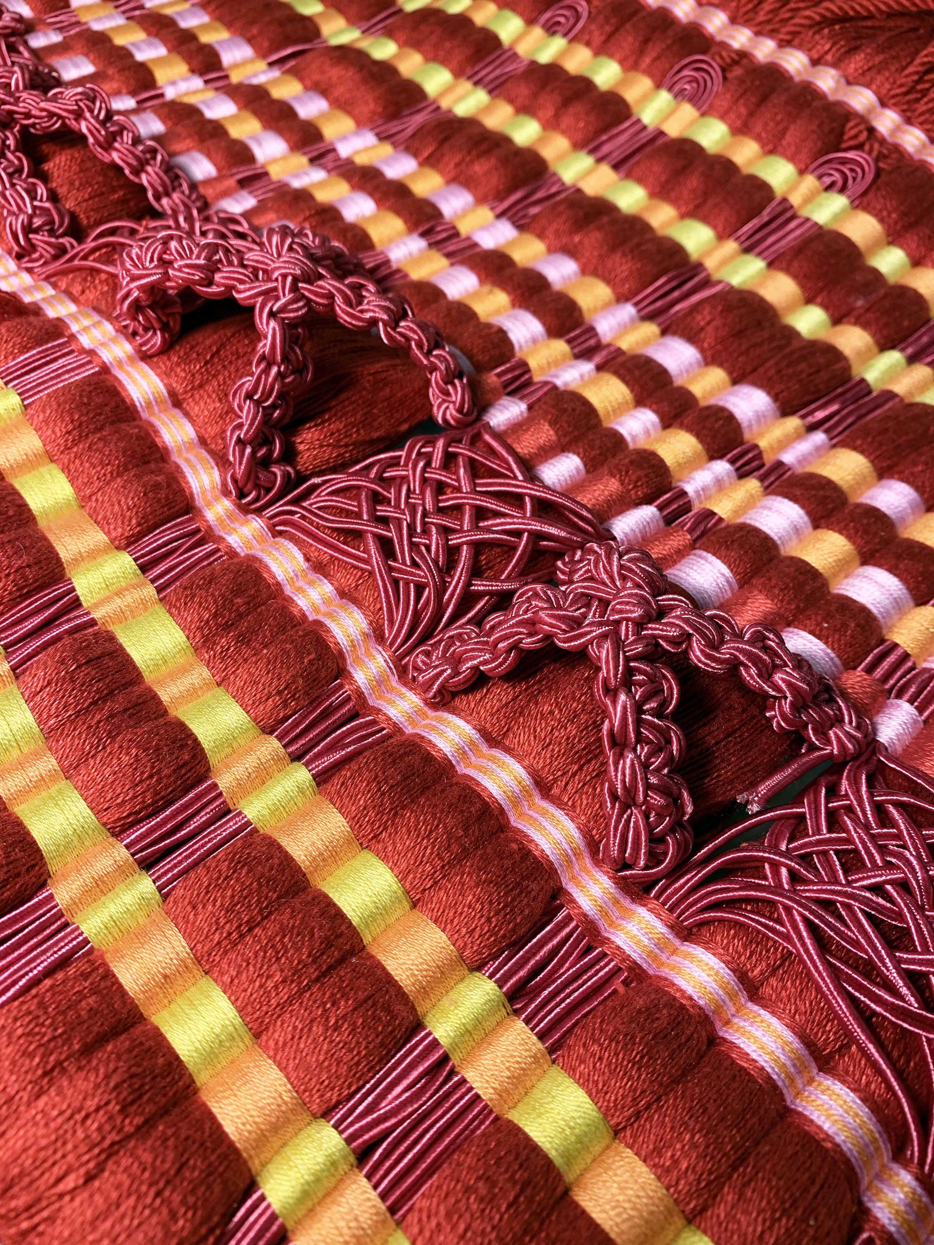 Hand-woven passementerie artwork featuring vibrant red and yellow patterns, showcasing Elizabeth Ashdown's distinctive weaving technique.