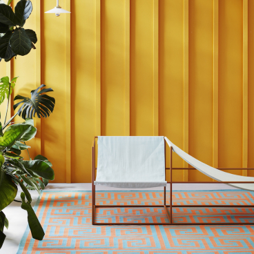 Mediterranean-inspired rug by Adam Nathaniel Furman displayed in a vibrant setting with modern furniture and plants.