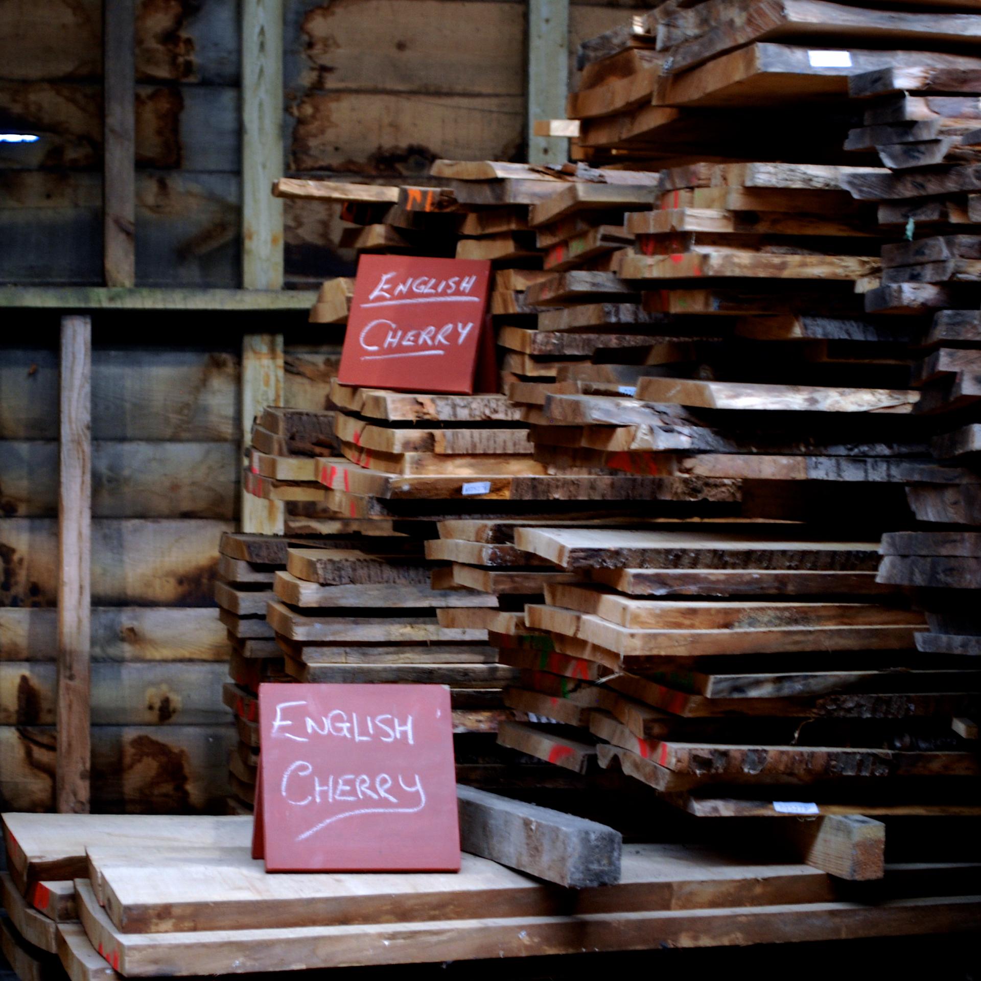 Stacks of English cherry wood slabs labeled for contemporary furniture making in a sustainable workshop setting.